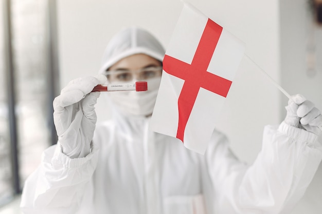 El científico en traje de overol con una muestra de coronavirus y una bandera inglesa