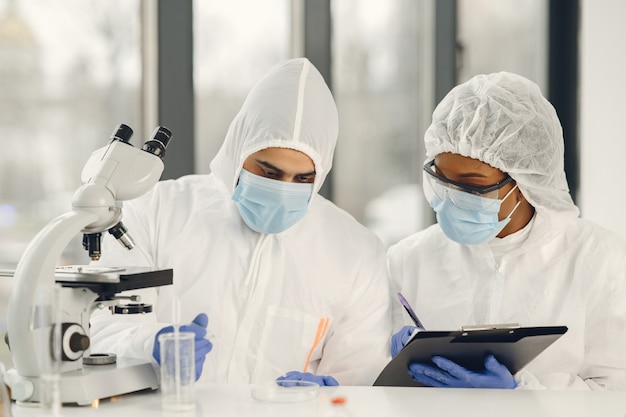 Científicos y microbiólogos con traje PPE y mascarilla sostienen el tubo de ensayo y el microscopio en el laboratorio, buscando tratamiento o vacuna para la infección por coronavirus. Covid-19, laboratorio y concepto de vacuna.