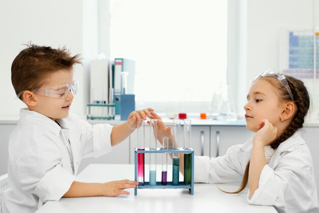 Científicos de niño y niña en el laboratorio con gafas de seguridad y tubos de ensayo