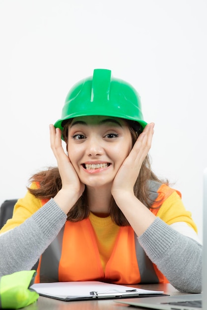 Foto gratuita cierra la foto de una trabajadora con chaleco y casco verde sonriendo a la cámara. foto de alta calidad