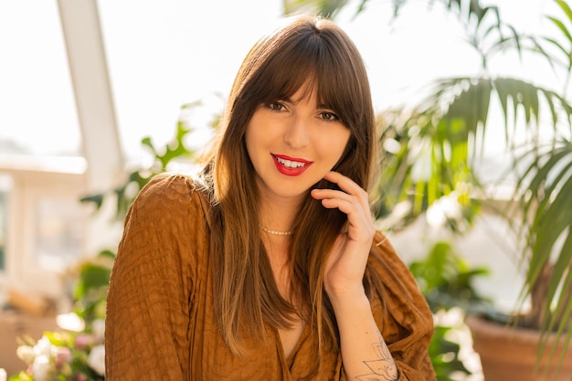 Cierra el retrato de una hermosa morena posando en un elegante salón bohemio con plantas caseras.