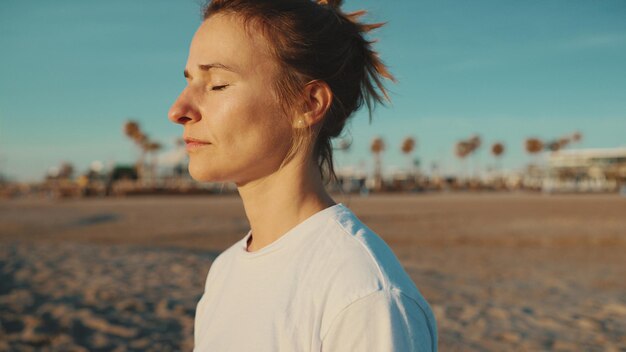 Cierra el retrato de una hermosa mujer rubia manteniendo los ojos cerrados meditando la práctica de yoga junto al mar