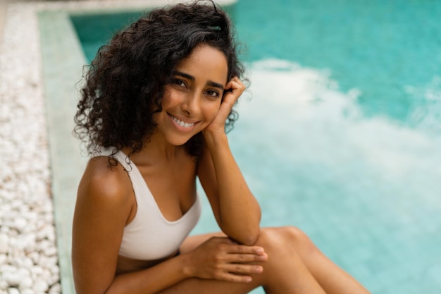 Cierra el retrato de una mujer bronceada sonriente con pelos rizados posando en la piscina. Concepto de verano y vacaciones.