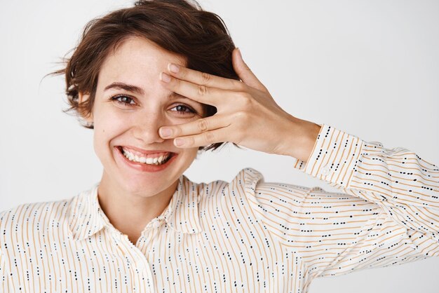 Cierra el retrato de una mujer hermosa con maquillaje natural que muestra una piel facial limpia e hidratada y sonríe a la cámara de pie sobre fondo blanco.