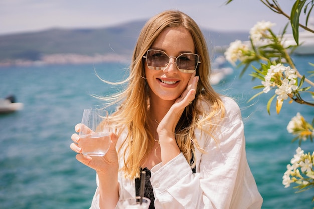 Cierra el retrato de verano de una mujer elegante y bonita rubia posando en el restaurante cerca de las vacaciones de lujo en el mar