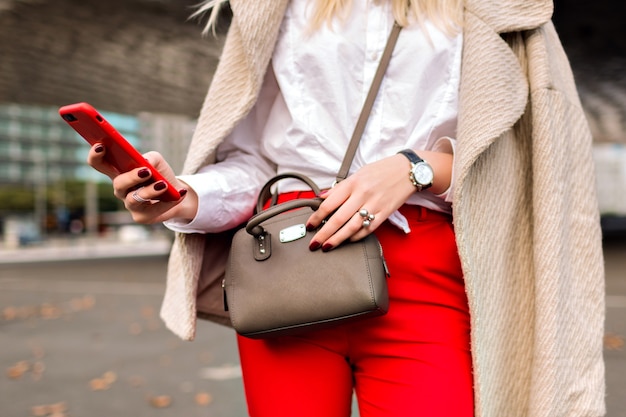 Cierre los detalles de moda, mujer de negocios, tocó algo en su teléfono, fondo urbano de otoño de la ciudad, traje brillante y abrigo de cachemira, listo para la conferencia.