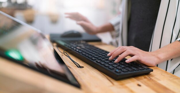 Cierre la mano femenina trabajando escribiendo información del teclado con el propietario del dispositivo de pantalla del monitor agregando datos para el análisis del concepto de ideas de estrategia empresarial