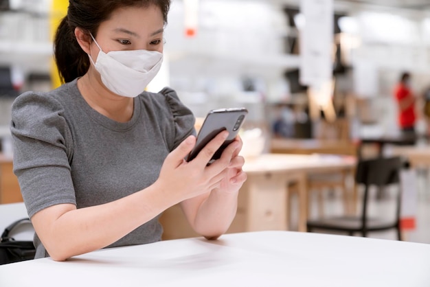 Cierre la mano de una mujer asiática usando la búsqueda de teléfonos inteligentes o navegue por las redes sociales en línea. Una mujer asiática en Internet se sienta en la cafetería del patio de comidas jugando juegos de teléfonos inteligentes en línea con diversión.