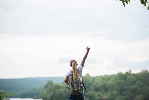 Cierre de la parte posterior de la muchacha turística con los brazos que crían felices con la naturaleza cerca del lago. Concepto de viaje