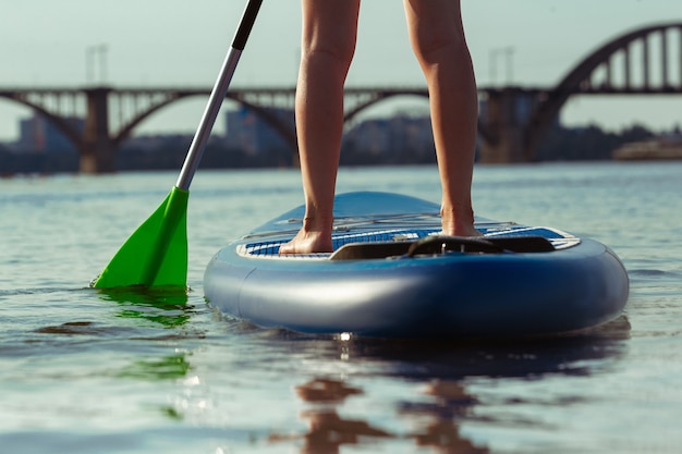 Cierre las piernas. Atractiva mujer joven de pie en paddle board, SUP.