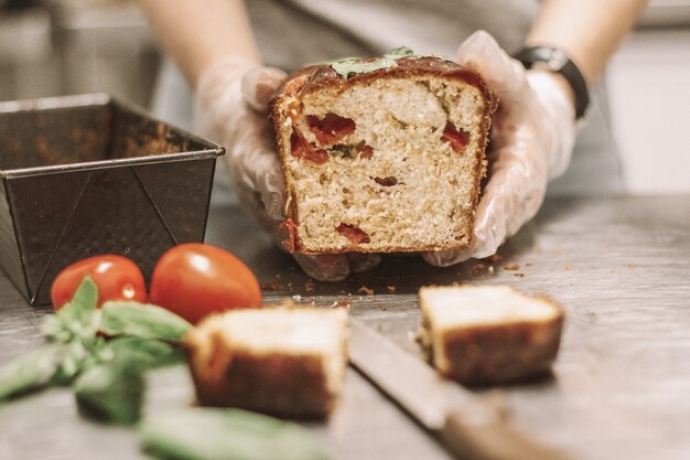 Cierre plano de chef sosteniendo una barra de pan cerca de tomates con un fondo borroso
