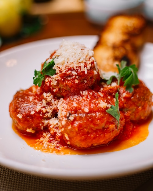 Cierre de plato de albóndigas adornado con salsa de tomate parmesano rallado y perejil