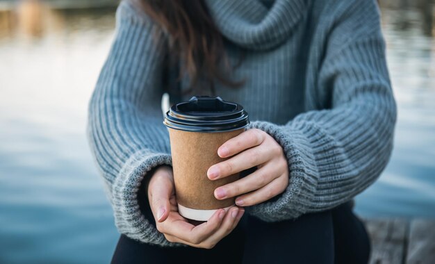 Cierre una taza de café en manos de una mujer en la naturaleza cerca del río