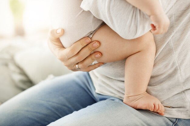 Ciérrese para arriba de la madre que celebra a su bebé recién nacido con la mano. Pierna de niño pequeño y gran mano cariñosa de madre. Escena familiar.