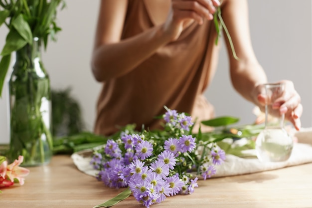 Ciérrese para arriba de las manos del florista que hacen el ramo de flores en el lugar de trabajo.