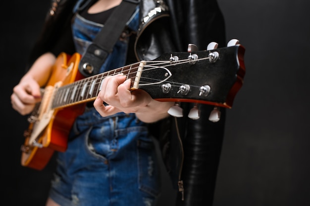 Ciérrese para arriba de las manos de la muchacha en la guitarra sobre fondo negro.