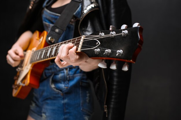 Ciérrese para arriba de las manos de la muchacha en la guitarra sobre fondo negro.