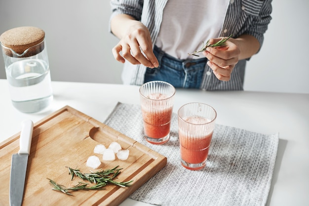 Ciérrese para arriba de las manos de la mujer que decoran el smoothie sano de la desintoxicación del pomelo con romero.