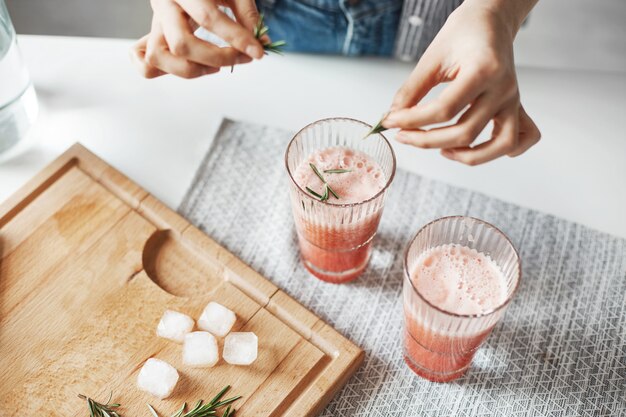 Ciérrese para arriba de las manos de la mujer que decoran el smoothie sano de la desintoxicación del pomelo con romero.