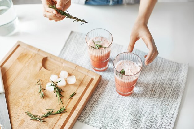 Ciérrese para arriba de las manos de la mujer que decoran el smoothie sano de la desintoxicación del pomelo con romero.