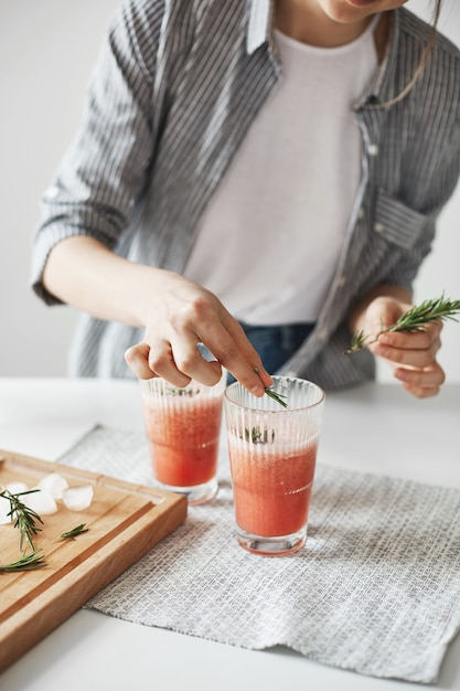 Ciérrese para arriba de las manos de la mujer que decoran el smoothie sano de la desintoxicación del pomelo con romero.