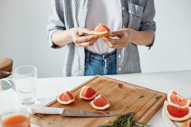 Ciérrese para arriba de la muchacha que lleva a cabo el pedazo del pomelo sobre la pared blanca. Concepto de nutrición saludable