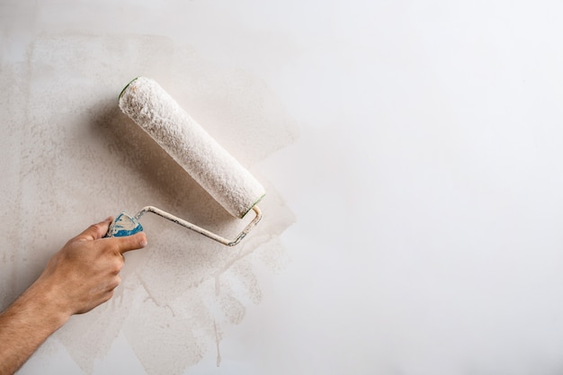 Ciérrese para arriba de la pared de la pintura de la mano con el rodillo.