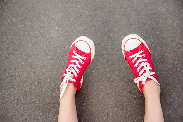 Ciérrese para arriba de piernas en los keds rojos que mienten en el asfalto.