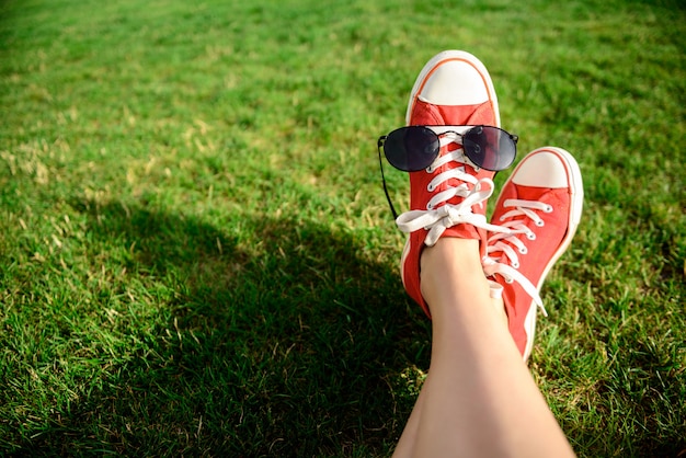 Ciérrese para arriba de piernas en los keds rojos que mienten en hierba.