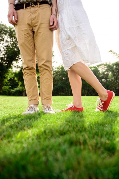 Ciérrese para arriba de las piernas de la pareja en keds en hierba.