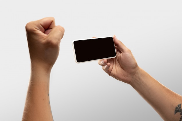 Ciérrese encima de las manos masculinas que sostienen el teléfono con la pantalla en blanco durante la observación en línea de partidos y campeonatos deportivos populares en todo el mundo.