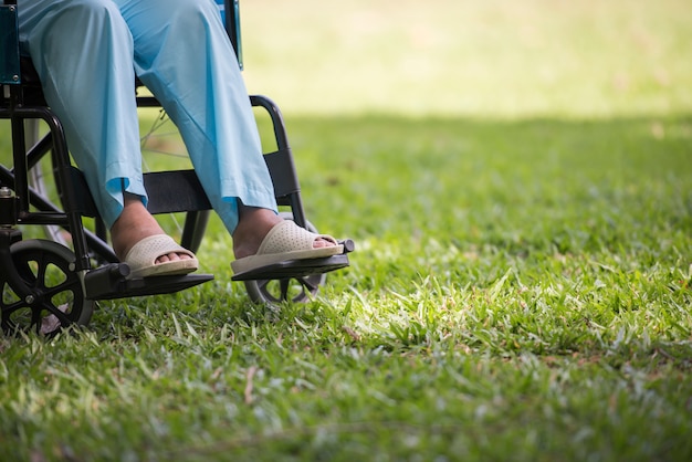 Ciérrese encima de la mujer mayor sola que se sienta en la silla de ruedas en el jardín en hospital