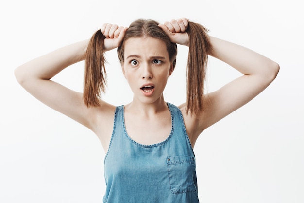 Foto gratuita ciérrese encima del retrato aislado de la muchacha divertida encantadora del estudiante caucásico con el pelo largo oscuro que corta ojos con la boca abierta, divirtiéndose, intentando hacer reír a la hermana.