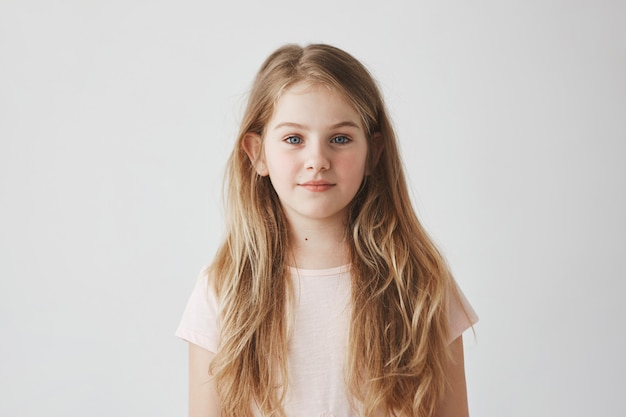 Ciérrese encima del retrato de la chica joven apuesta con el pelo rubio en vestido rosado, con la expresión tranquila, posando para la sesión de fotos en la escuela.