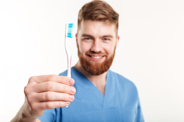 Ciérrese encima del retrato de un dentista de sexo masculino sonriente que muestra el cepillo de dientes