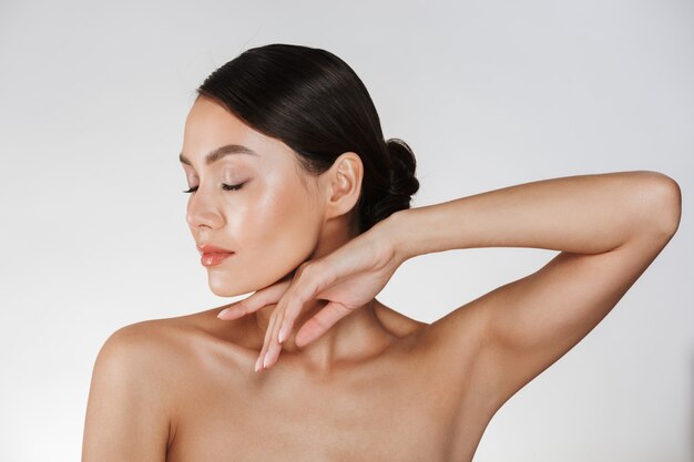 Ciérrese encima del retrato del estudio de la mujer morena con la piel limpia con los ojos cerrados, aislado sobre blanco