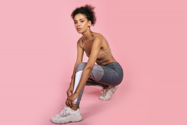 Ciérrese encima del retrato del estudio de la mujer negra hermosa con los pelos afro que hacen ejercicios en estudio en fondo rosado.