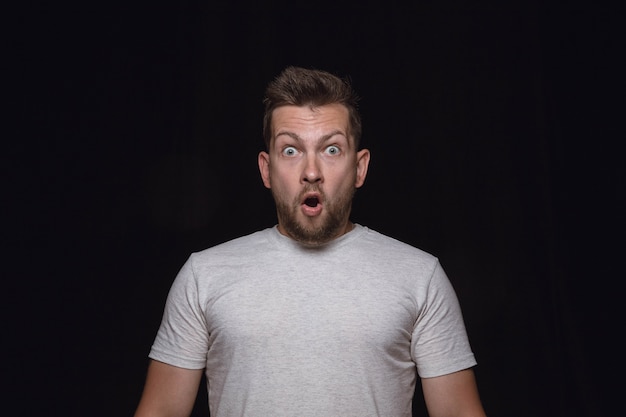 Foto gratuita ciérrese encima del retrato del hombre joven aislado en la pared negra del estudio. emociones reales del modelo masculino. preguntándose, emocionado y asombrado. expresión facial, concepto de emociones humanas.