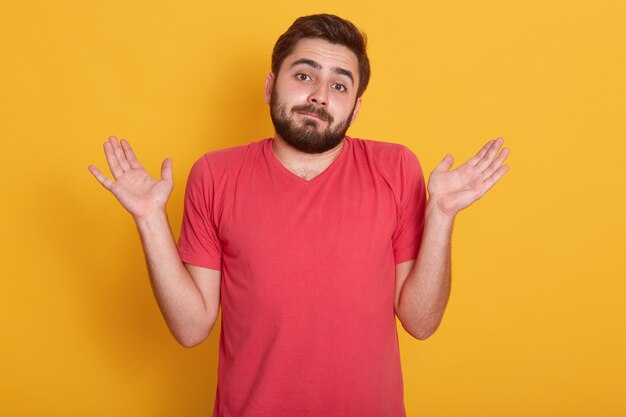 Ciérrese encima del retrato del hombre joven asombrado en la presentación casual roja de la camiseta aislada sobre amarillo