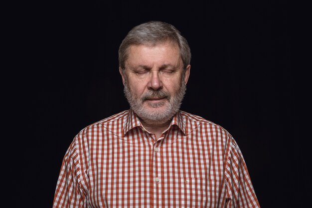 Ciérrese encima del retrato del hombre mayor aislado en el espacio negro. Pensando y sonriendo