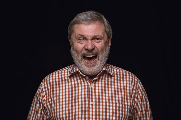 Foto gratuita ciérrese encima del retrato del hombre mayor aislado en la pared negra. emociones reales del modelo masculino. llorando a través de la risa y la sonrisa. expresión facial, concepto de emociones humanas.