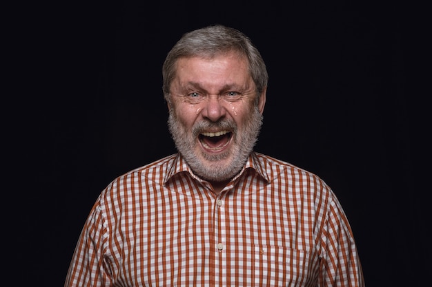 Ciérrese encima del retrato del hombre mayor aislado en la pared negra. emociones reales del modelo masculino. Llorando a través de la risa y la sonrisa. Expresión facial, concepto de emociones humanas.