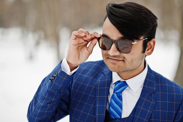 Ciérrese encima del retrato del hombre de negocios indio elegante en traje y gafas de sol que se presentan en el día de invierno al aire libre