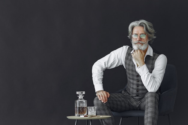 Ciérrese encima del retrato del hombre pasado de moda sonriente. Gentelman sentado en una silla. Abuelo con un vaso de whisky.