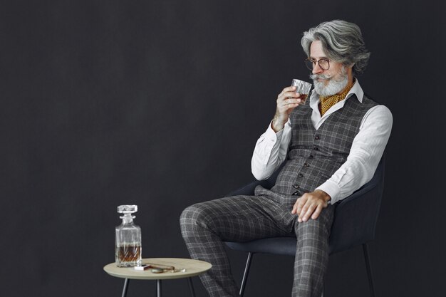 Ciérrese encima del retrato del hombre pasado de moda sonriente. Gentelman sentado en una silla. Abuelo con un vaso de whisky.