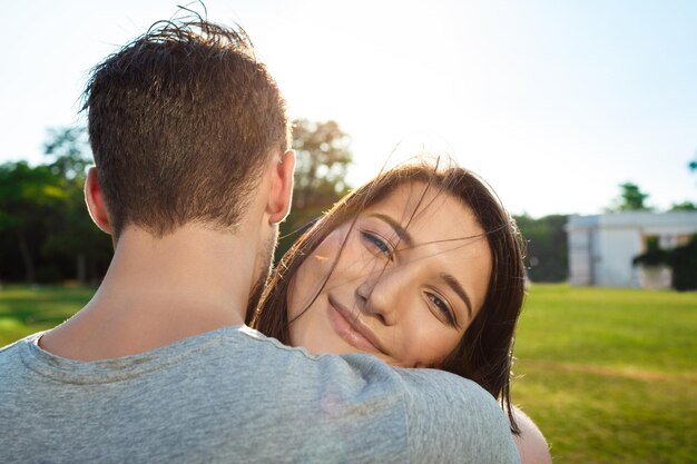 Ciérrese encima del retrato de la joven pareja hermosa sonriendo, relajándose, abrazando en el parque.