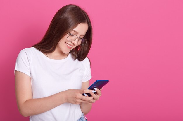 Ciérrese encima del retrato del mensaje que mecanografía de la mujer adorable a sus amigos o marido. Joven mujer sosteniendo teléfono móvil