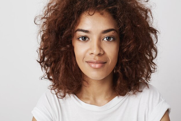 Ciérrese encima del retrato de la muchacha africana hermosa con los ojos grandes que sonríe con una sonrisa que siente confianza y calma, siendo convincente y atractivo.