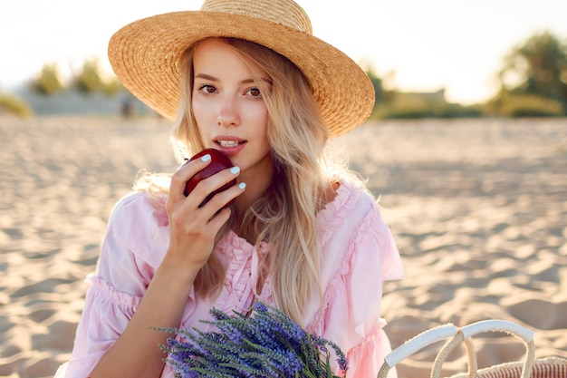 Ciérrese encima del retrato de la muchacha blanca natural en el sombrero de paja que disfruta los fines de semana cerca del océano. Posando con frutas. Ramo de lavanda en bolsa de paja.