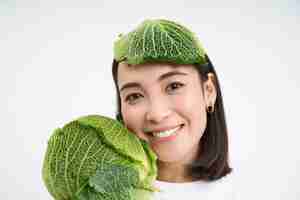 Foto gratuita ciérrese encima del retrato de la mujer asiática linda con la hoja de lechuga en la cabeza que sonríe y que muestra el repollo verde wh